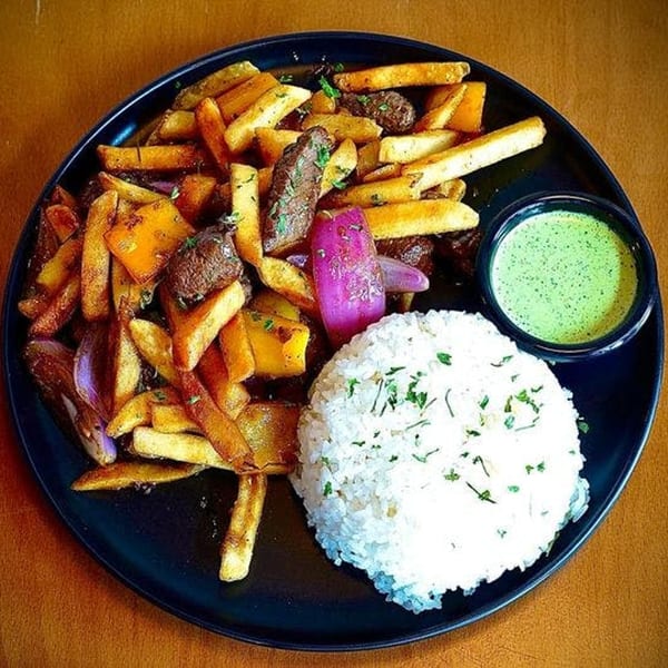 Vietnamese dish with steak, french fries, red onion, rice, and a side of green sauce.