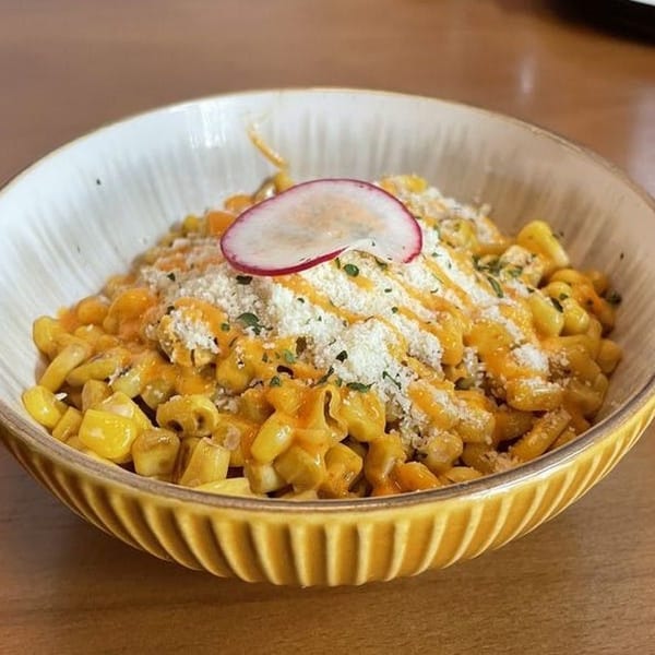 Vietnamese street corn in a yellow bowl, topped with cheese, sauce, and a radish slice.