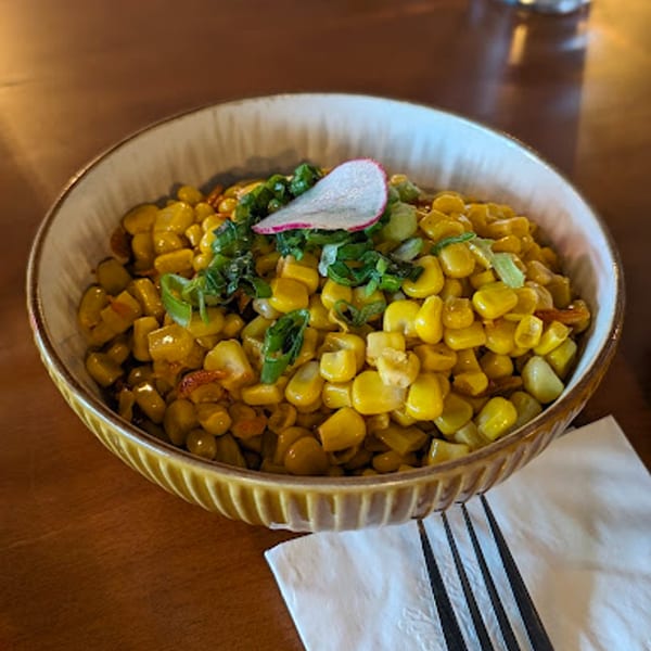 Vietnamese corn dish with green onions and a radish slice in a brown bowl on a wooden table.