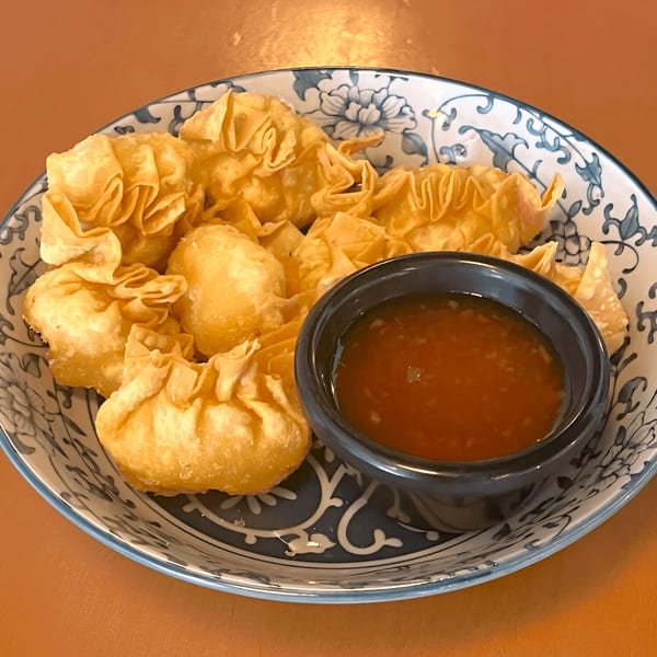 Golden fried wontons with a side of sweet chili dipping sauce in a decorative bowl.